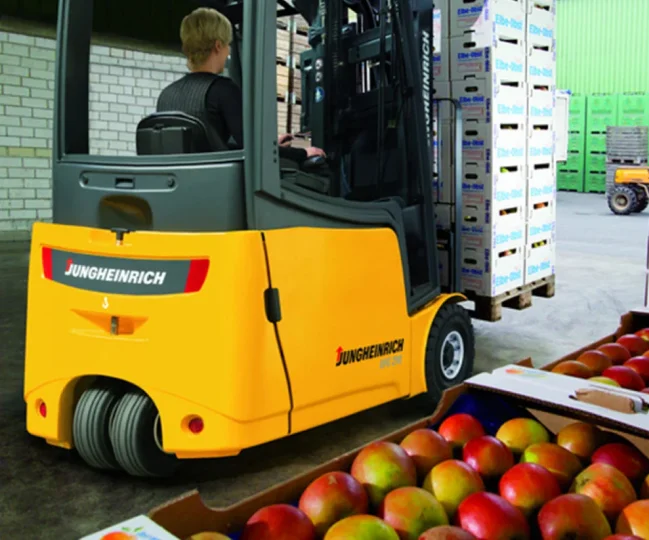 Forklift loading palletized produce and farm supplies near a covered packing shed
